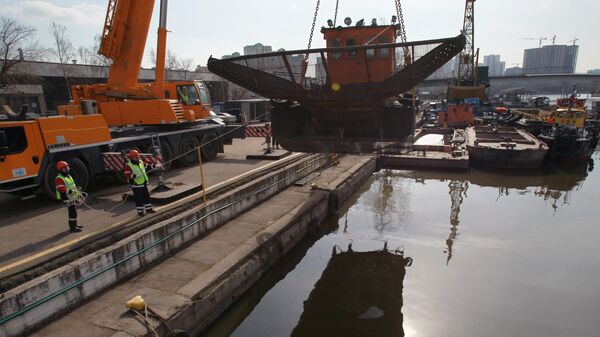 Сотрудники ГУП Мосводосток спускают на воду мусоросборное судно во время подготовки к открытию технической навигации на Москве-реке