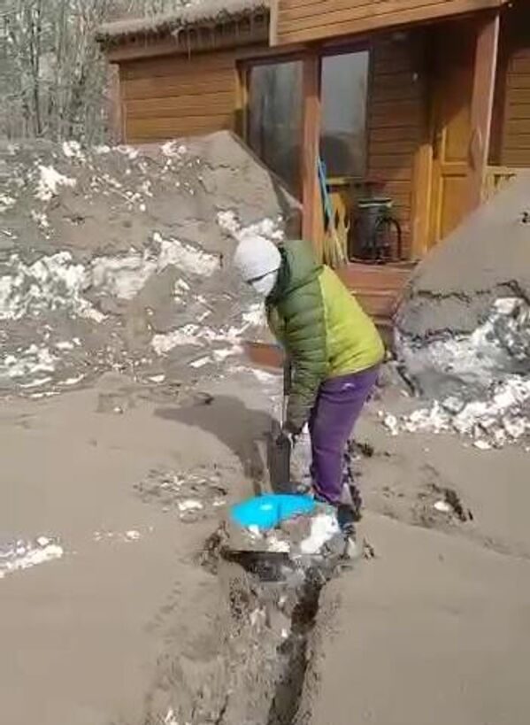 Местная жительница расчищает участок, занесенный пеплом в результате извержения вулкана Шивелуч в Усть-Камчатском районе