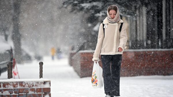 Девушка идет по улице во время апрельского снегопада в Новосибирске