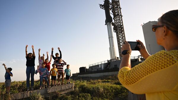 Люди фотографируются на фоне космического корабля SpaceX Starship, стоящего на стартовой площадке перед летными испытаниями в Бока-Чика, штат Техас