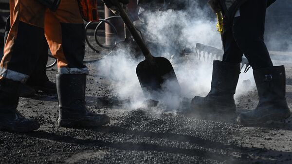 Рабочие заделывают яму во время поддерживающего ремонта дорог