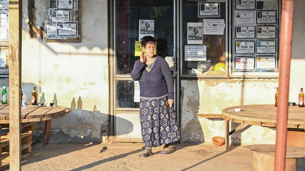 Местная жительница стоит около магазина в окне которого развешаны некрологи в деревне Дубона, где произошла стрельба