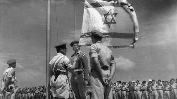 Израильский офицер поднимает национальный флаг во время празднования создания государства Израиль после его провозглашения 14 мая 1948 года