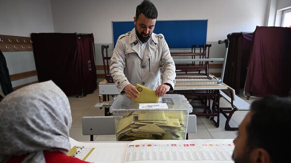 Избиратель опускает бюллетени в урну на избирательном участке во время голосования на всеобщих выборах в Стамбуле