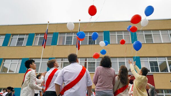 Выпускники отпускают воздушные шарики в цветах триколора на празднике Последний звонок во дворе МБОУ Средняя школа № 65 города Мариуполя