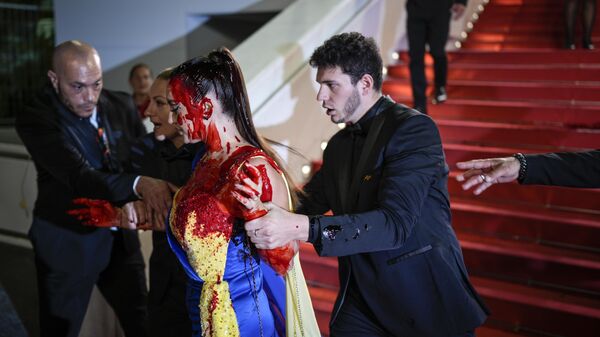 Охрана уводит женщину в платье под цвет украинского флага с красной дорожки Каннского кинофестиваля, 2023 год 