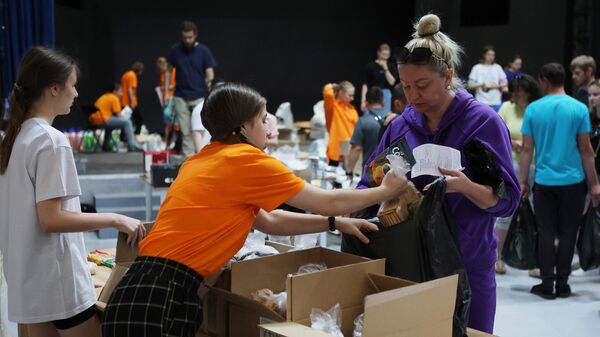 Женщина и волонтеры в пункте сбора и выдачи гуманитарной помощи эвакуированным жителям города Шебекино в Центре молодежных инициатив в Белгороде