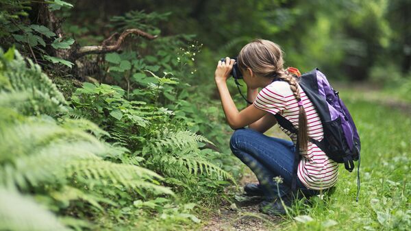 Девочка фотографирует растение в парке