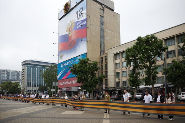 Жители города держат полотно георгиевской ленты во время празднования Дня России на Главной Городской площади Краснодара