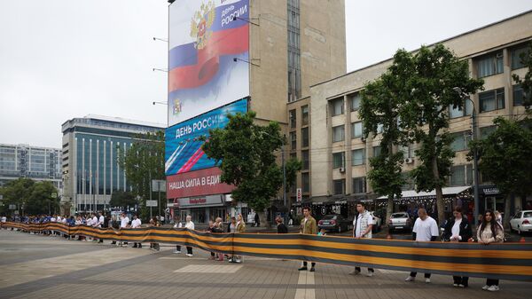 Жители города держат полотно георгиевской ленты во время празднования Дня России на Главной Городской площади Краснодара