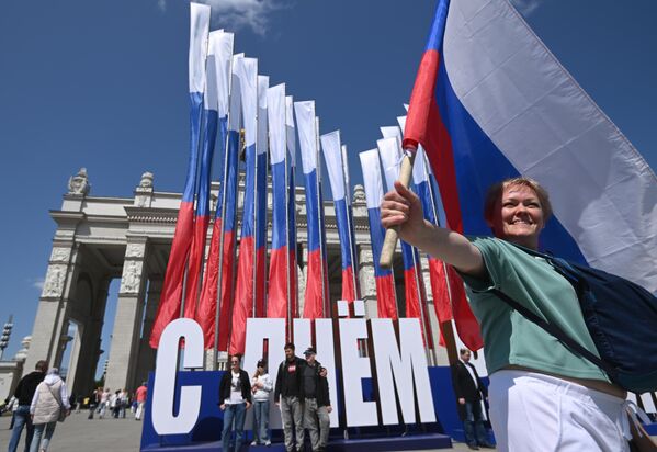 Женщина с флагом фотографируется у входа на ВДНХ во время празднования Дня России в Москве