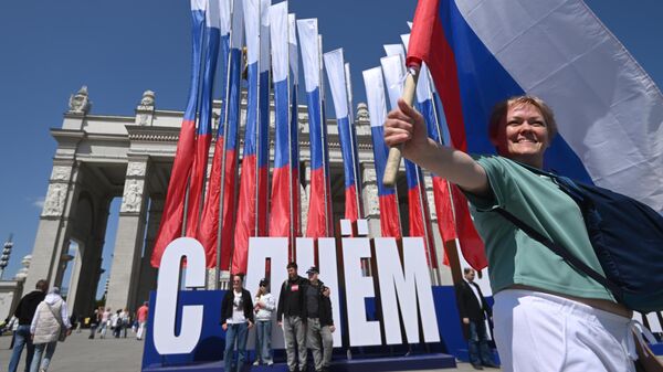 Женщина с флагом фотографируется у входа на ВДНХ во время празднования Дня России в Москве