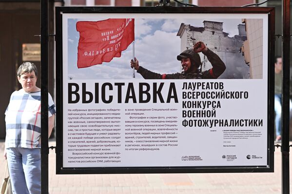 Женщина смотрит фотографии, представленные на выставке победителей Всероссийского конкурса военной фотожурналистики на Арбате в Москве