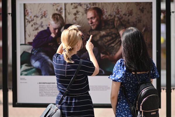 Девушки смотрят фотографии, представленные на выставке победителей Всероссийского конкурса военной фотожурналистики на Арбате в Москве