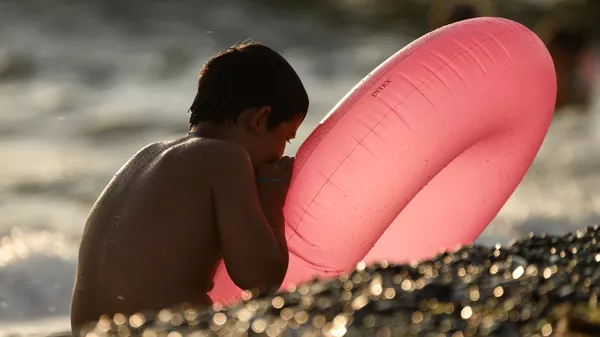 Мальчик надувает круг на пляже в поселке Новофедоровка в Крыму.