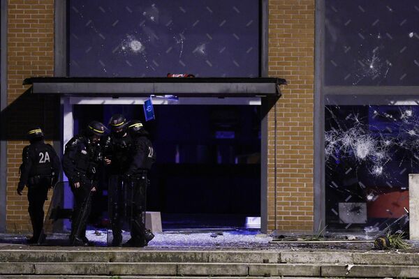 Полицейские стоят перед разбитыми окнами фасада театра во время протестов в Рубе, на севере Франции, 30 июня 2023 года