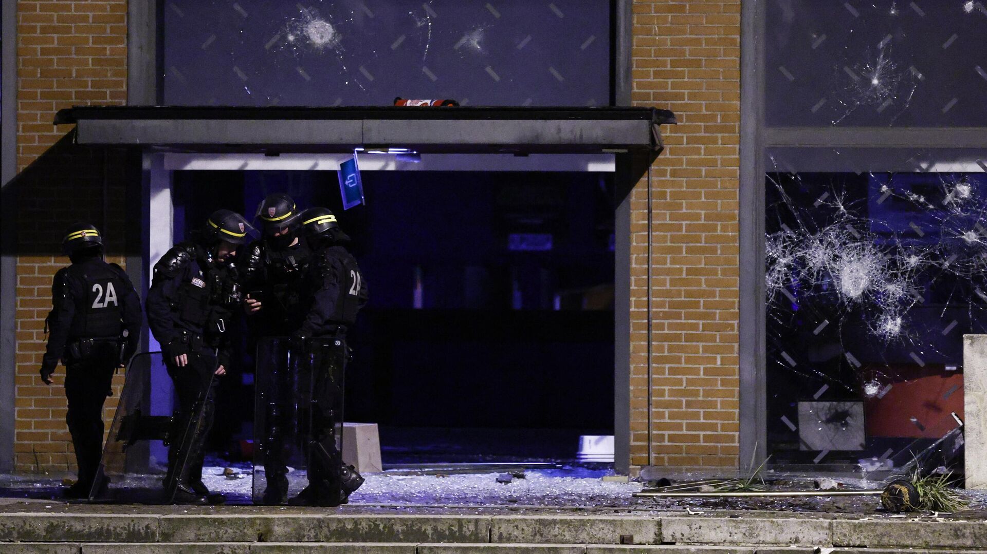 Полицейские стоят перед разбитыми окнами фасада театра во время протестов в Рубе, на севере Франции, 30 июня 2023 года - РИА Новости, 1920, 30.06.2023