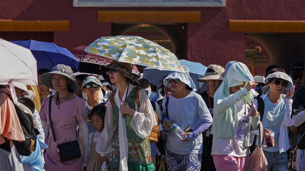 Посетители прячутся от жары под зонтиками, покидая Запретный город в Пекине