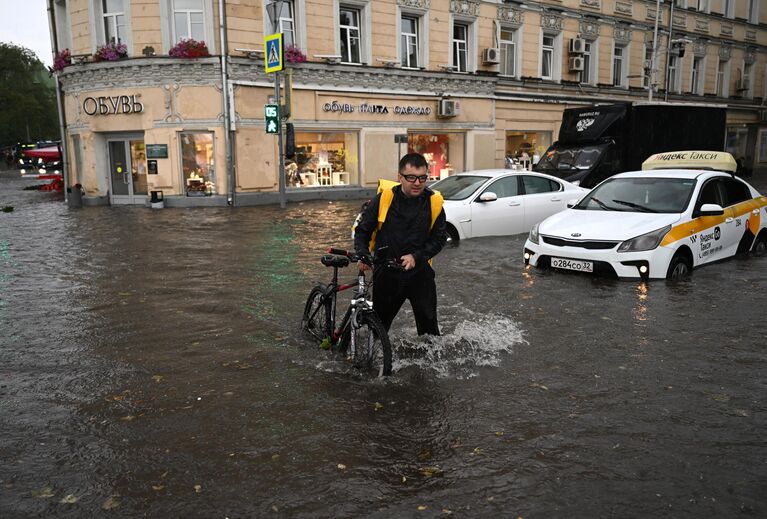 Мужчина с велосипедом на подтопленной улице в результате ливня в Москве