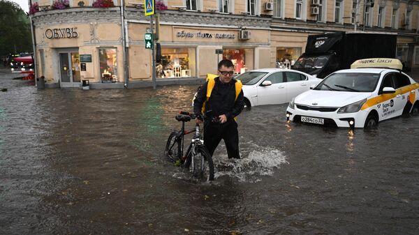 Мужчина с велосипедом на подтопленной улице в результате ливня в Москве