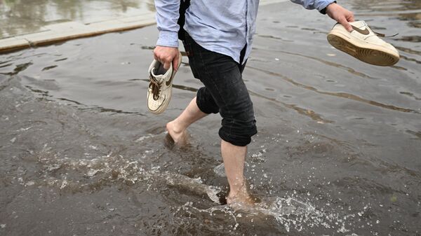 Прохожий идет по подтопленной улице, сняв свою обувь
