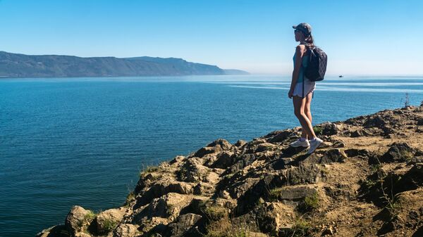 Девушка стоит на краю Шаманского мыса у озера Байкал