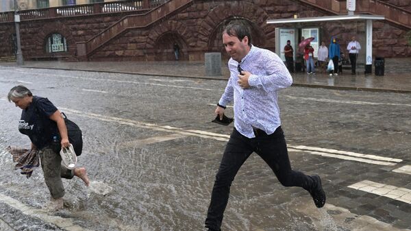 Мужчина перепрыгивает поток воды на подтопленной дороге в результате ливня в Москве