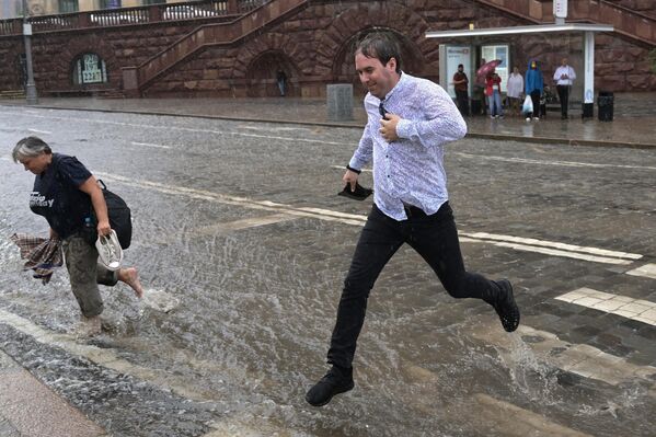 Мужчина перепрыгивает поток воды на подтопленной дороге в результате ливня возле метро Баррикадная в Москве