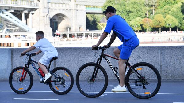 Мужчина с ребенком катаются на велосипедах по набережной Москвы