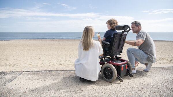 Родители с ребенком в инвалидном кресле на берегу моря