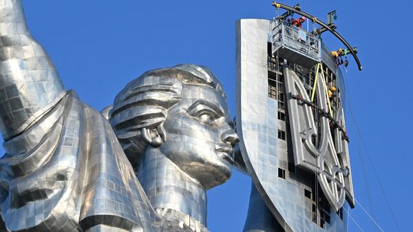 Рабочие устанавливают герб Украины на монумент Родина-мать в Киеве