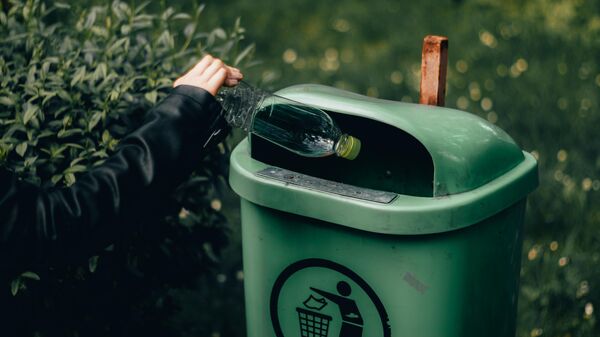 Девушка выбрасывает пластиковую бутылку в мусорный контейнер