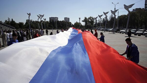 Участники праздничных мероприятий, приуроченных ко Дню российского флага, разворачивают 100-метровый флаг России на площади Ленина в Мариуполе