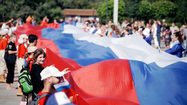 Участники праздничных мероприятий, приуроченных ко Дню российского флага, разворачивают 100-метровый флаг России на площади Ленина в Мариуполе