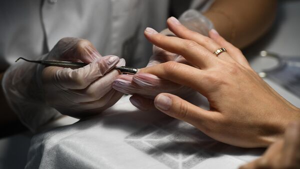 Мастер ногтевого сервиса обрабатывает ногти в салоне красоты