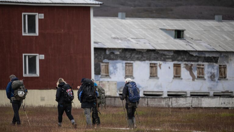 Туристы у заброшенных строений в городе Пирамида на архипелаге Шпицберген