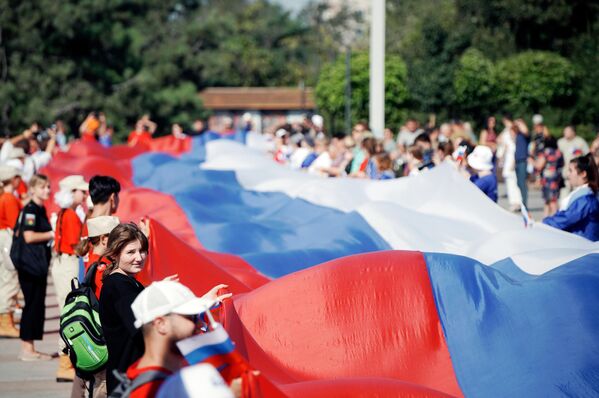 Участники праздничных мероприятий, приуроченных ко Дню российского флага, разворачивают 100-метровый флаг России на площади Ленина в Мариуполе