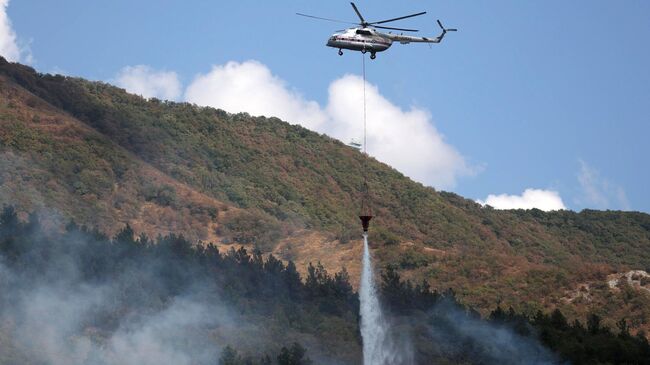 Вертолет сбрасывает воду на месте тушения лесного пожара