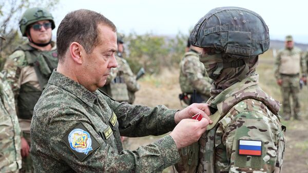 Заместитель председателя Совета безопасности РФ Дмитрий Медведев награждает бойца ВС РФ во время посещения полигона подготовки военнослужащих, набранных по контракту
