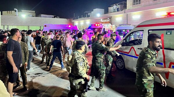 Военные и сотрудники служб экстренной помощи рядом с машинами скорой помощи, перевозящими раненых в больницу после пожара в округе Хамдания в Ираке