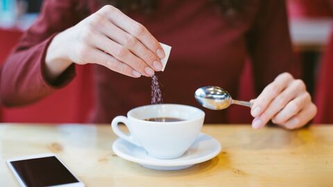 Девушка насыпает сахар в кофе