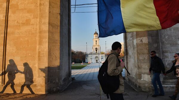 Люди идут под триумфальной аркой рядом с флагом Молдавии в Кишиневе