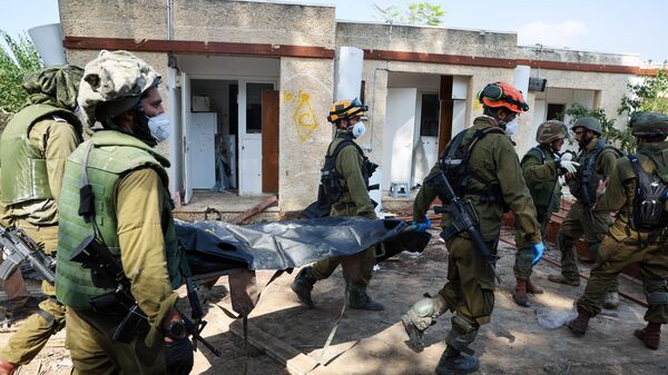 Израильские военные несут тело убитого во время атаки палестинских боевиков в Кфар-Азе. 10 октября 2023
