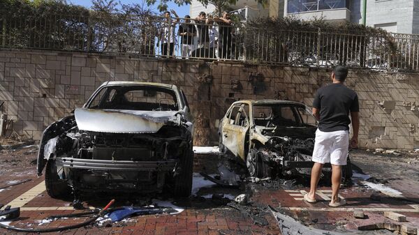 Израильтяне осматривают автомобили после попадания в них ракеты, выпущенной из сектора Газа