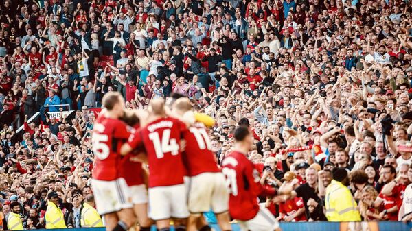 Футболисты Манчестер Юнайтед и болельщики на трибунах стадиона Олд Траффорд