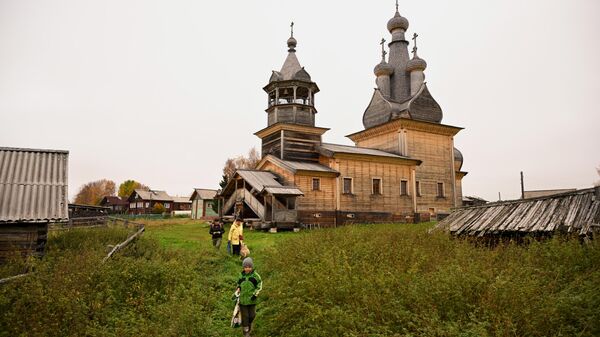 Местные жители идут по деревне Кимжа в Мезенском районе Архангельской области. На заднем плане - Одигитриевская церковь