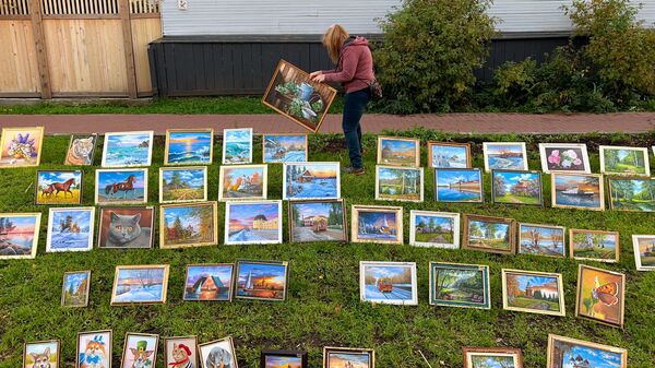Продавец расставляет картины на ярмарке в центре Архангельска