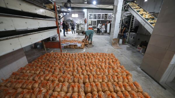 Сотрудники пекарни упаковывают хлеб, чтобы накормить палестинцев, стоящих в очереди на улице в Рафахе на юге сектора Газа