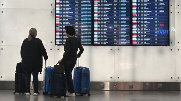 Пассажиры возле электронное табло вылетов в аэропорту
