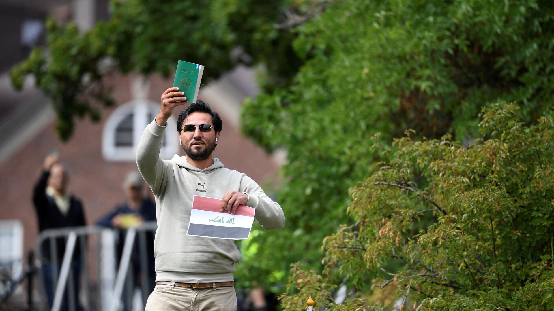 Иракский иммигрант Салван Момика держит Коран и лист бумаги с изображением флага Ирака во время акции протеста возле посольства Ирака в Стокгольме - РИА Новости, 1920, 20.10.2023
